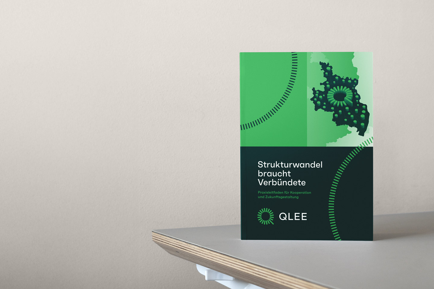 Cover des Hefts "Praxisleitfaden für Kooperation und Zukunftsgestaltung" von QLEE aufrecht stehend auf einem Tisch.